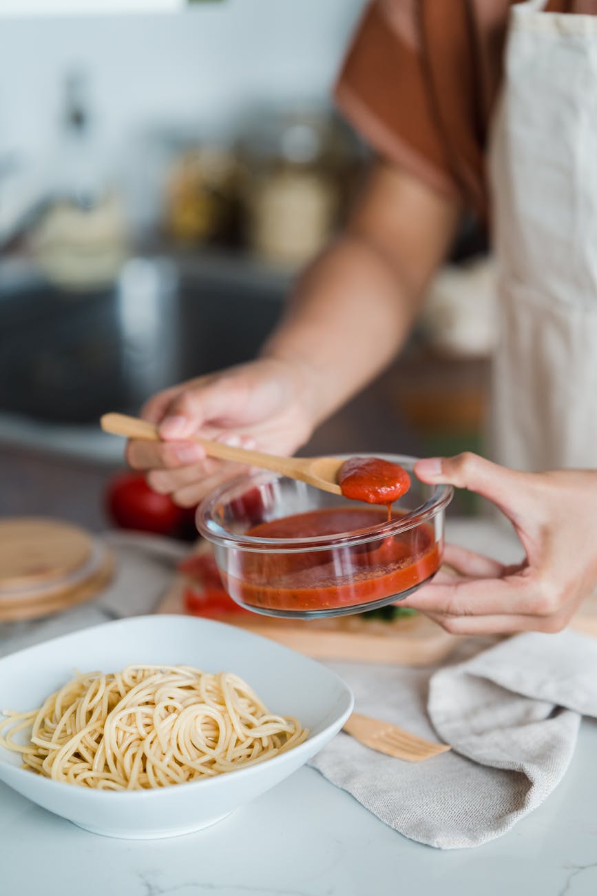 a person putting tomato sauce in a pasta
