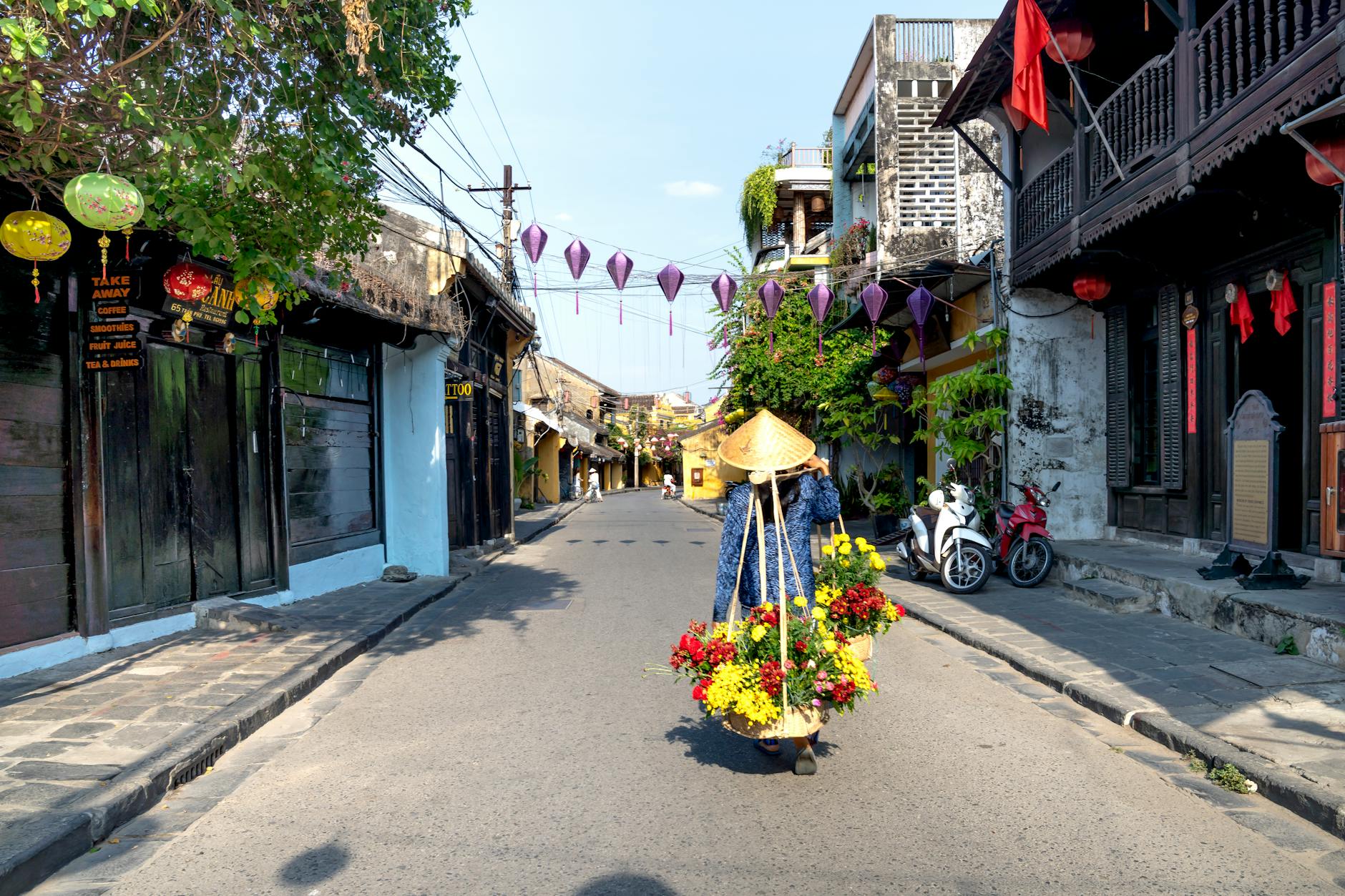asian woman in conical hat strolling on street with flowers