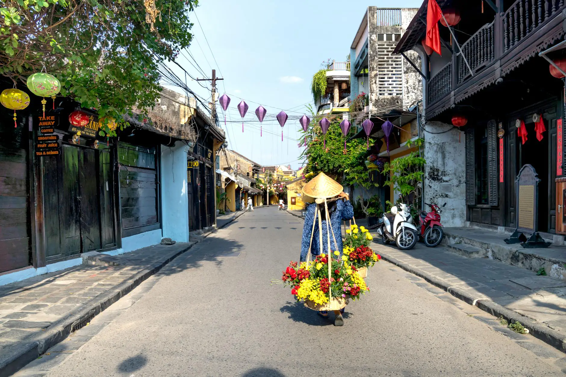 asian woman in conical hat strolling on street with flowers