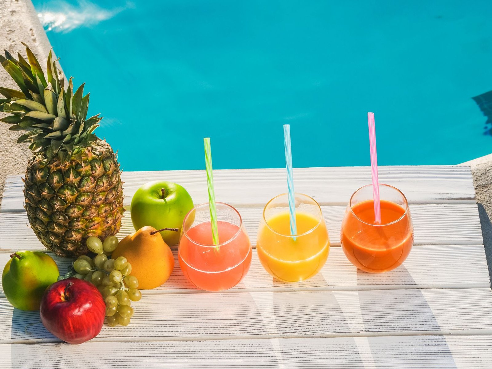 fruits and fruit drinks with straws in a row by a swimming pool